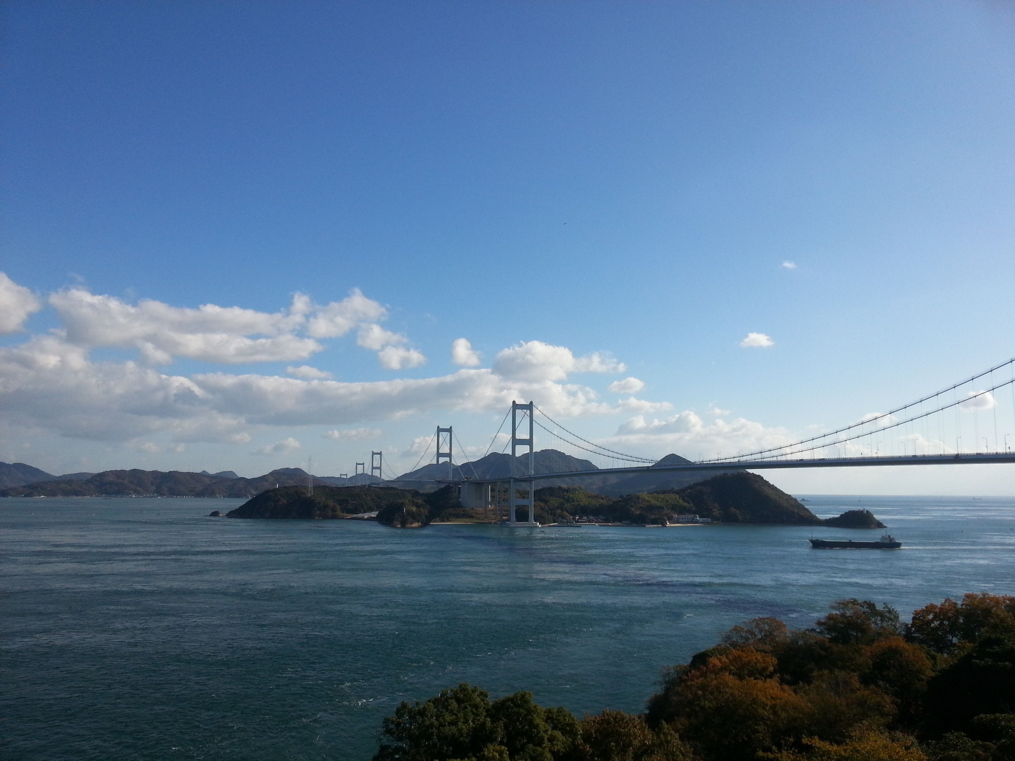 A suspension bridge over a body of water with multiple islands, surrounded by mountains.