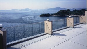 A balcony with a glass railing overlooking a body of water, a distant island, and mountains. - Daichoso (Imabari)