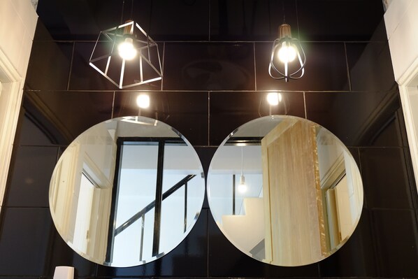 A modern interior with two large circular mirrors on a dark wall, a staircase, and geometric pendant lights. - Sleep Owl Hostel (Bangkok)