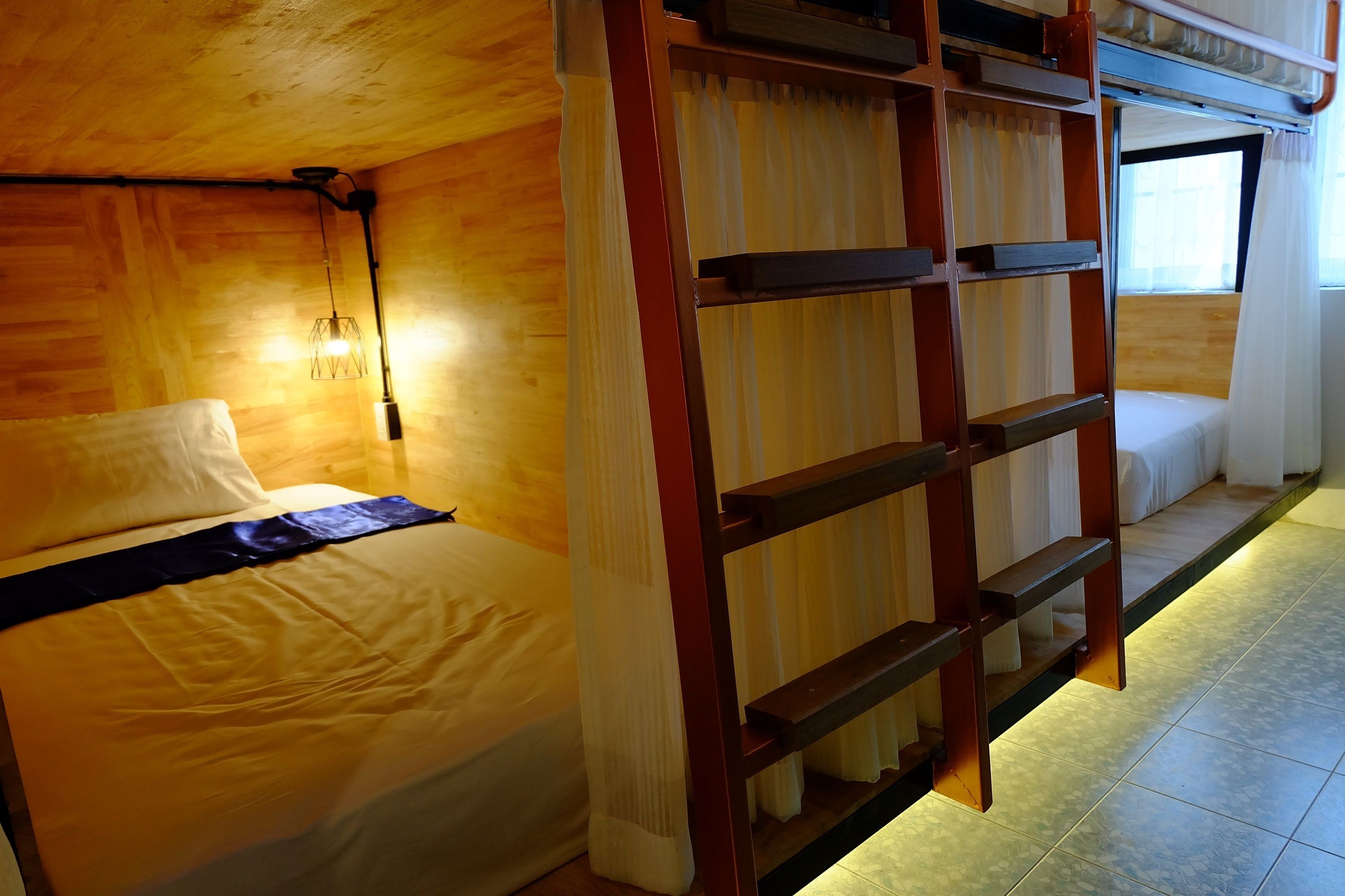 A bunk bed room with a wooden ceiling, a ladder, and a window with curtains.