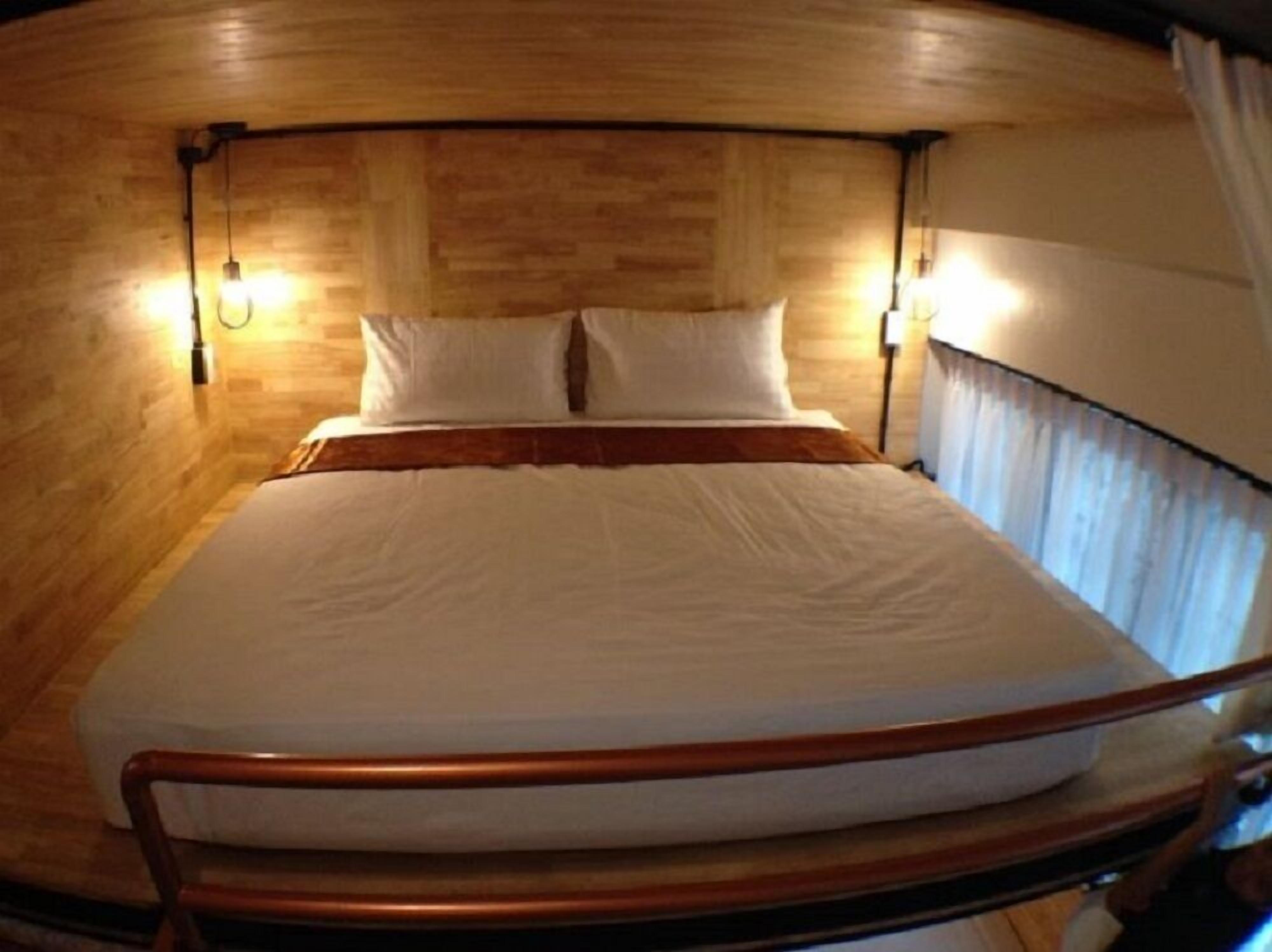 Una cama compacta con cabecera de madera y dos lámparas de noche en una habitación tipo cabaña con paredes de madera.