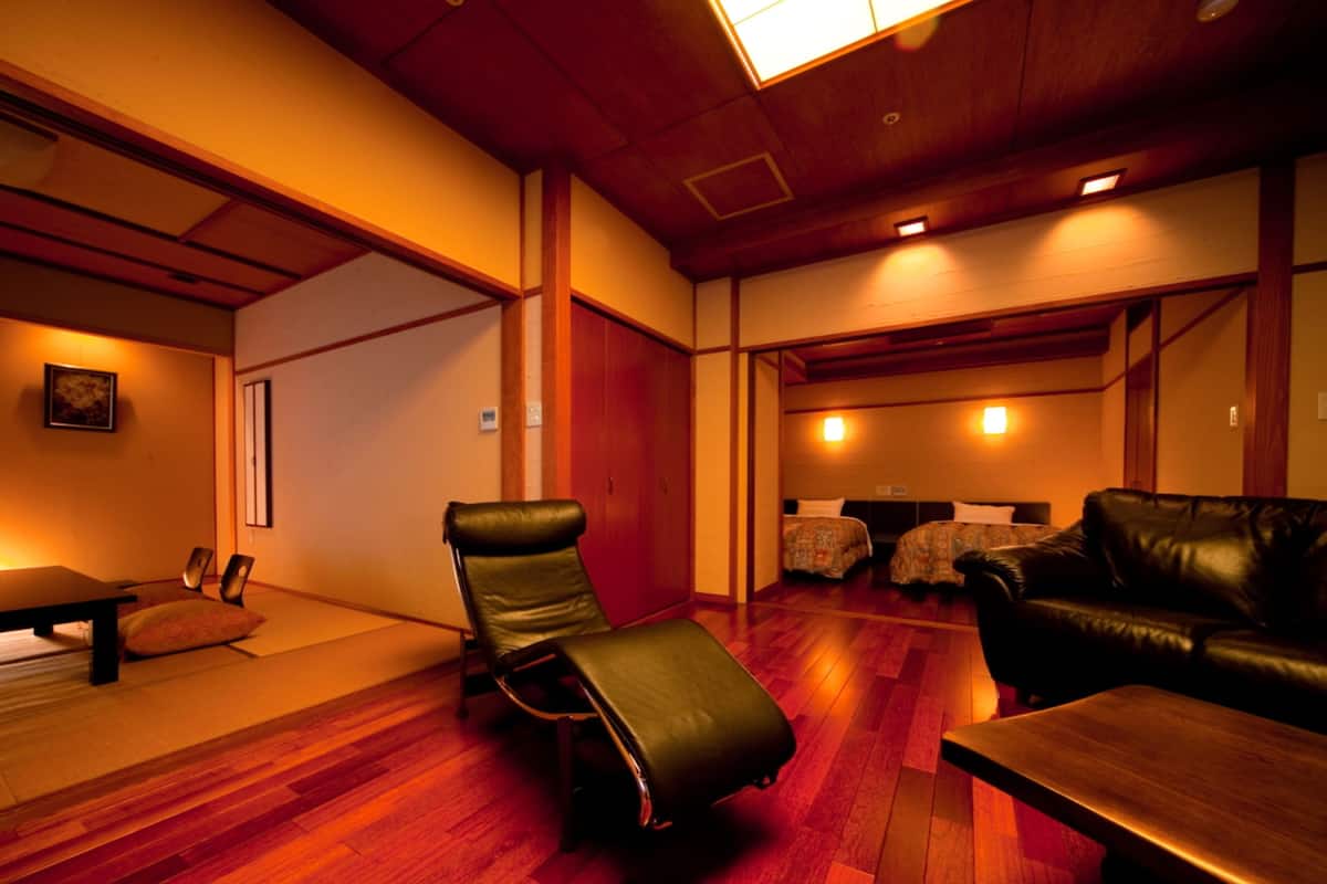 A room with a wooden floor, a leather chair, a sofa, and a small table.