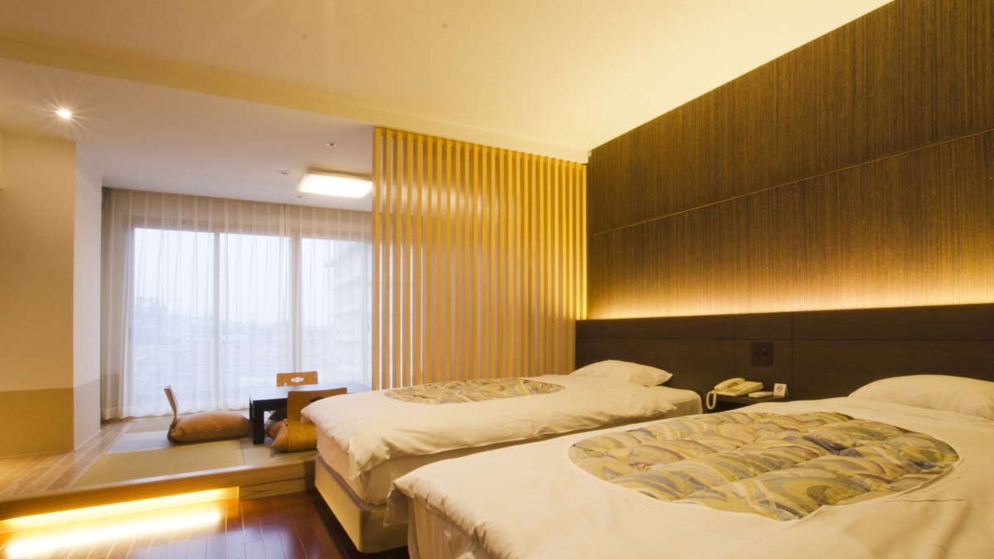 A hotel room with two beds, a desk, a chair, and a window with curtains.