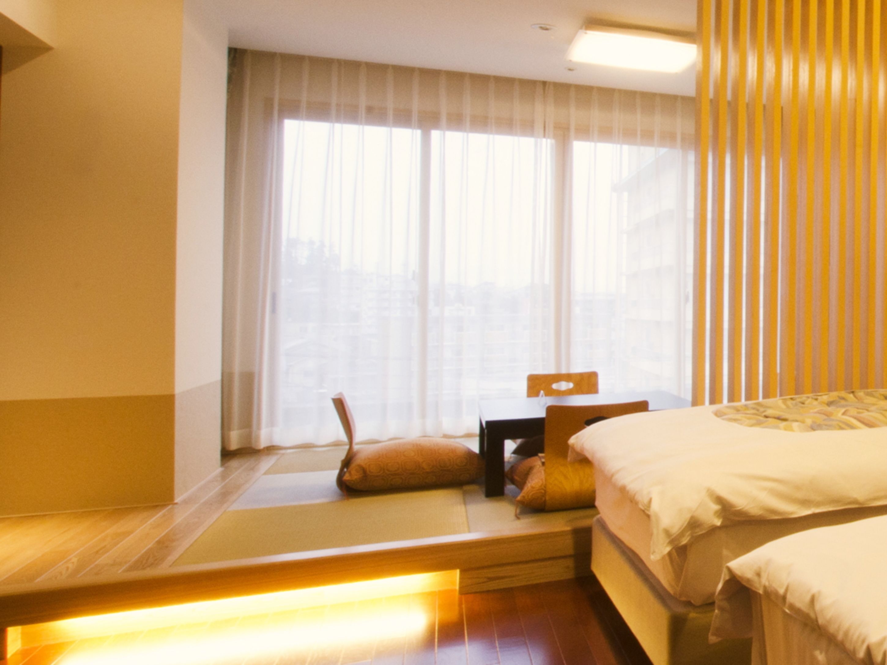 A hotel room with a bed, a bedside table, a chair, and a window with curtains.