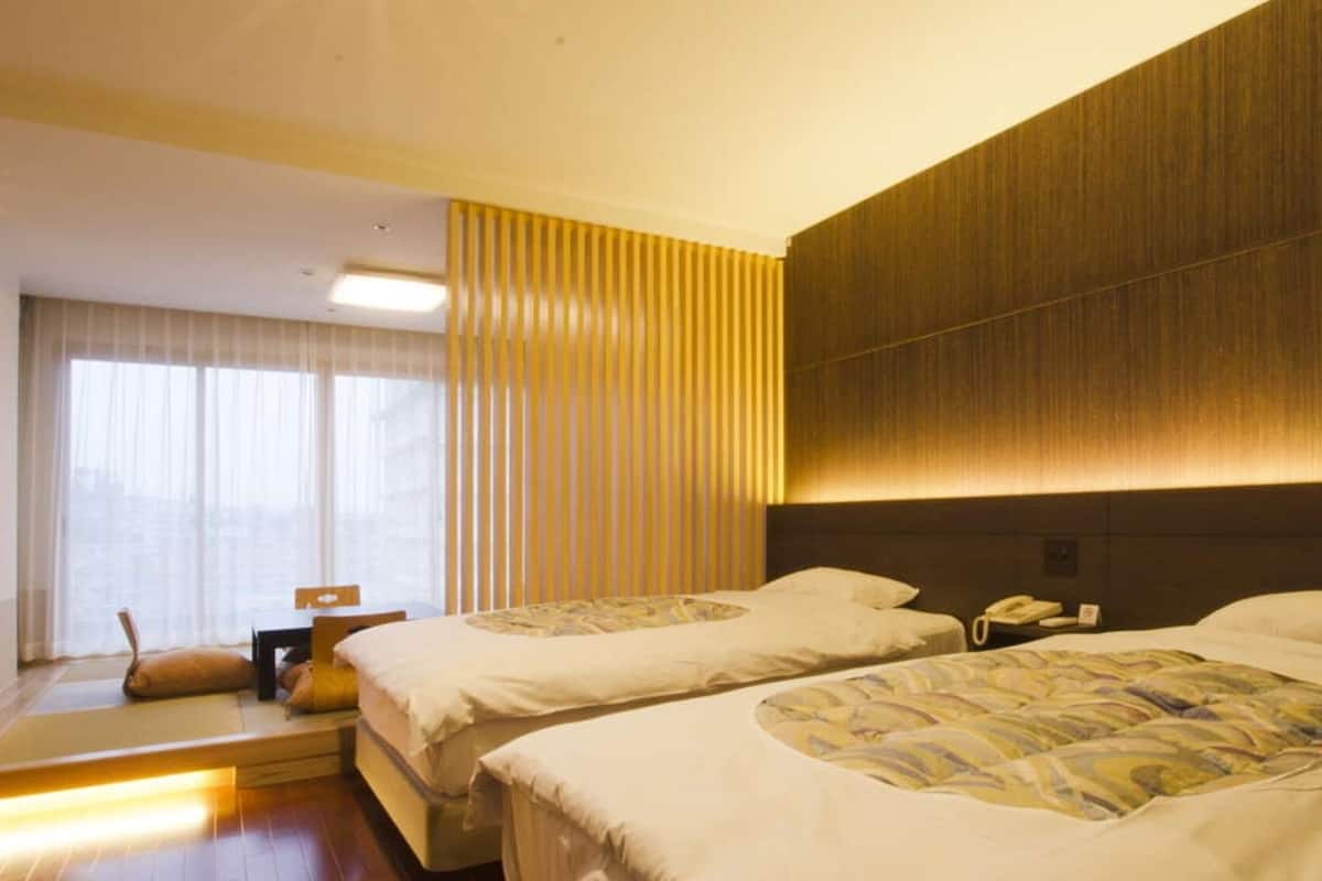 A hotel room with two beds, a desk, a chair, and a window with curtains.