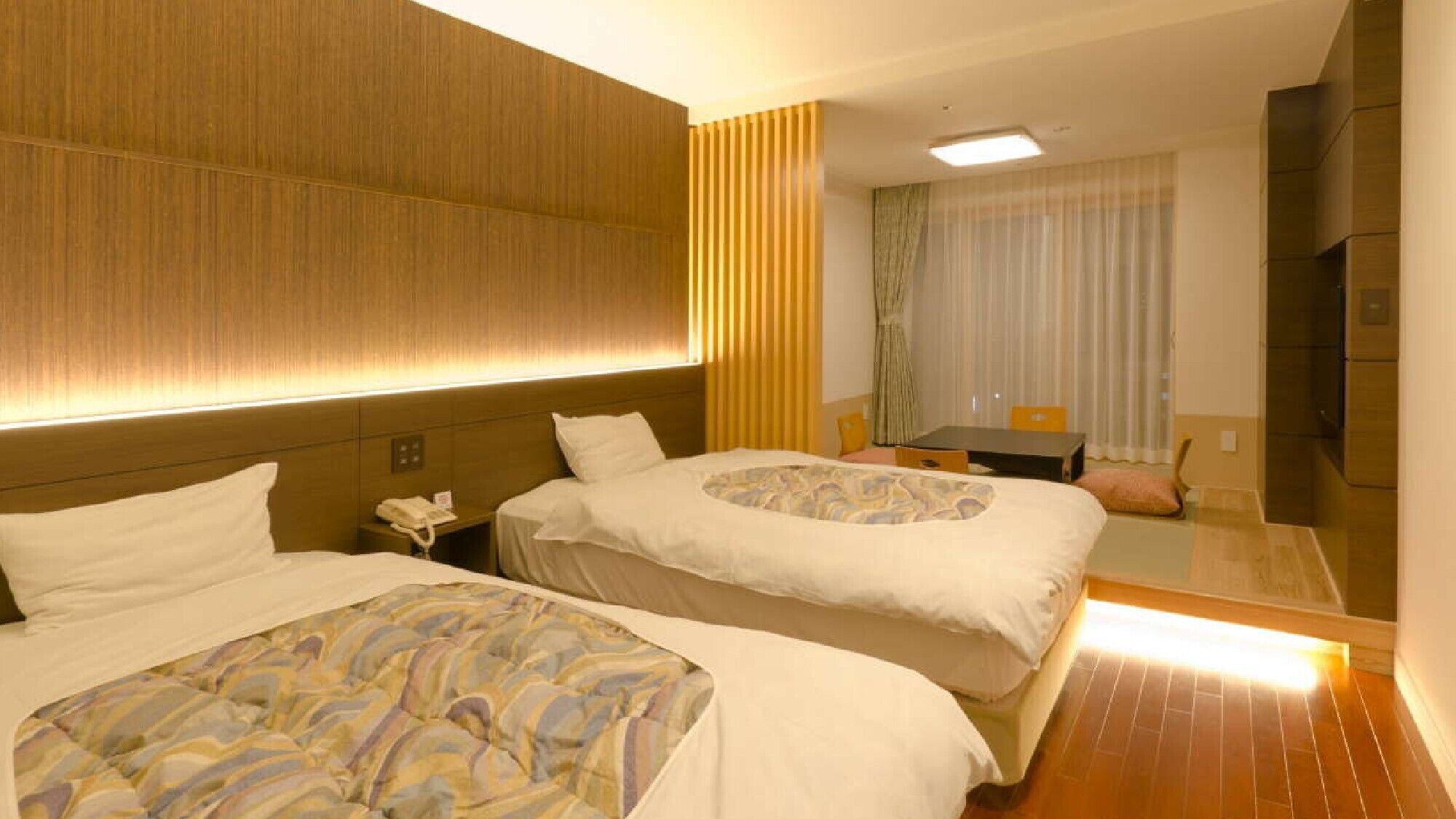 A hotel room with two beds, a desk, a chair, a phone, and a mirror.