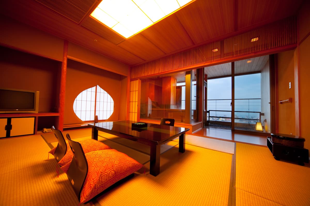 A traditional Japanese-style room with tatami flooring, a low table, and a sliding door leading to a balcony.