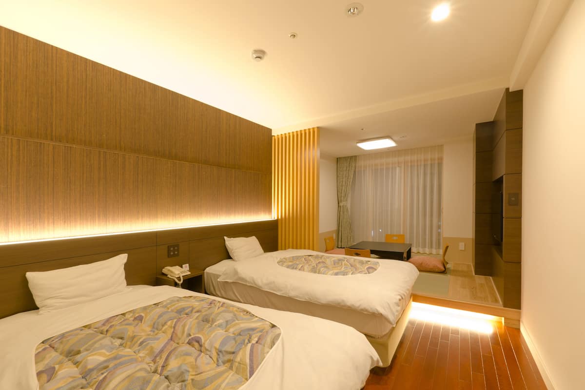 A hotel room with two beds, a desk, a chair, a telephone, and a mirror.