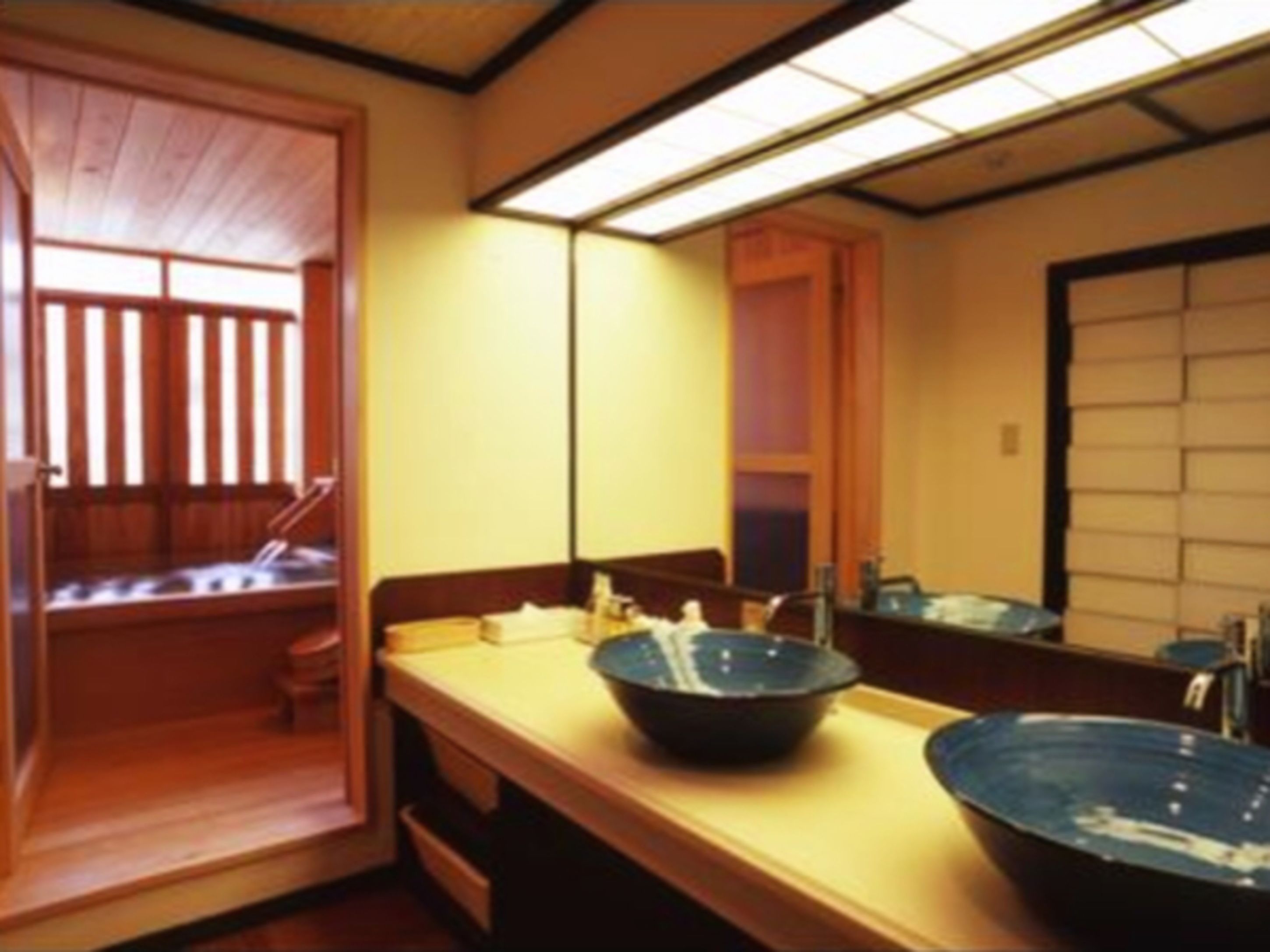 Ein traditioneller japanischer Raum mit einer Holztür, einer Holzbank, einem großen Spiegel und einem Holztisch mit einer Schale.