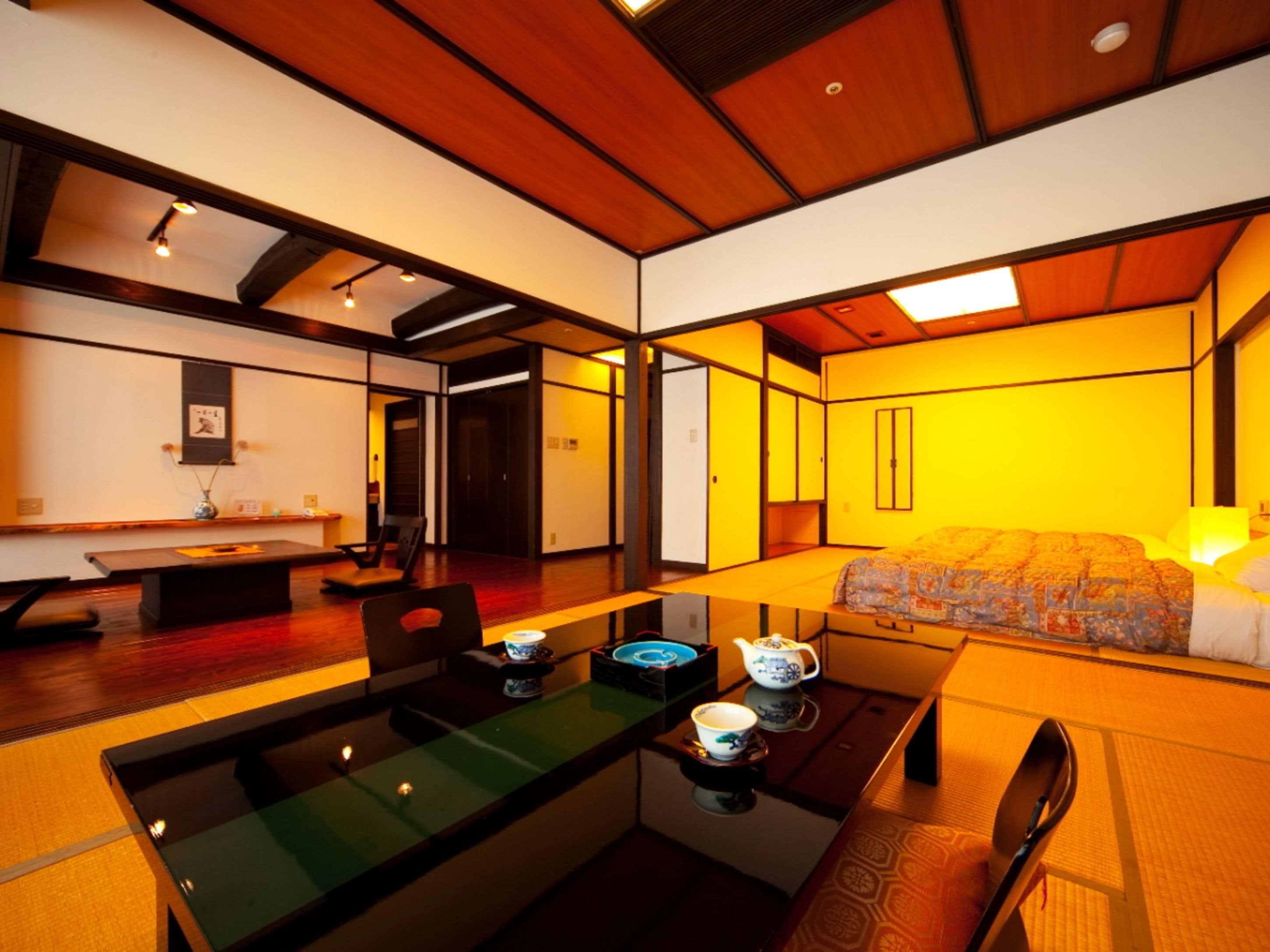 A traditional Japanese-style room with tatami flooring, a low table with tea set, and a bed with a patterned bedspread.