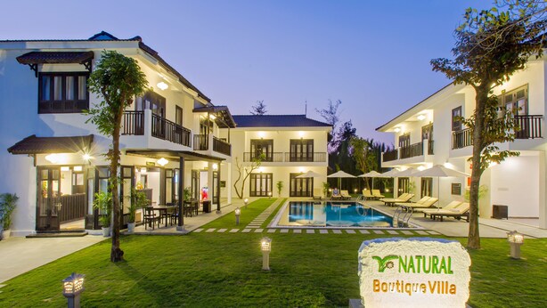 Una villa con piscina, mobiliario exterior y un letrero que dice "NATURAL Boutique Villa".