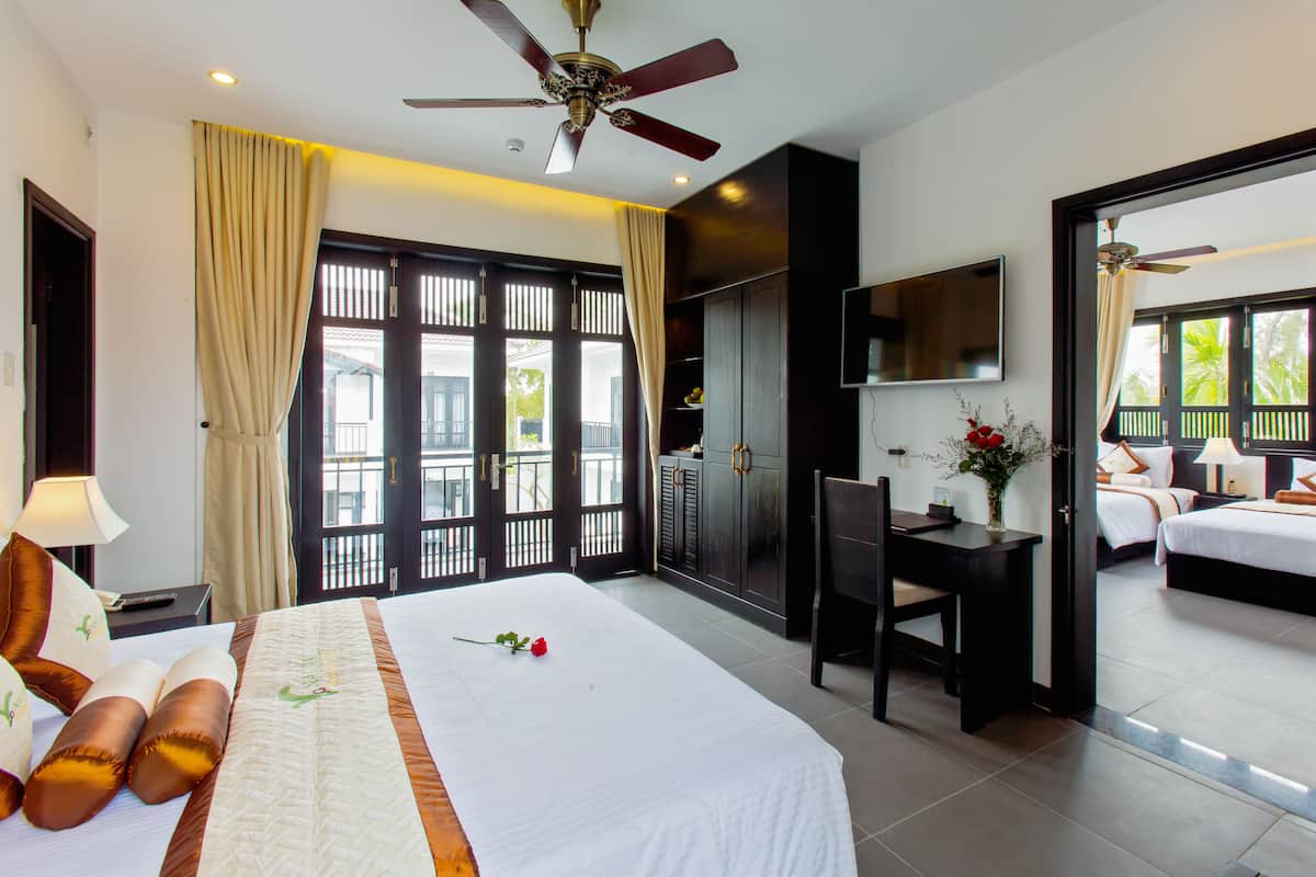 A hotel room with a large bed, a desk, a chair, a TV, and a balcony with a view.