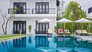 Un hotel moderno con zona de piscina, mobiliario exterior y un edificio de dos plantas con balcones.