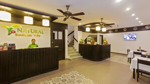 Zona de recepción con mostrador, una escalera y un comedor con mesas y sillas.