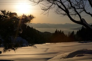 A snowy landscape with a clear path, trees, and distant mountains under a sunset. - Ryokan Warabino (Takayama)