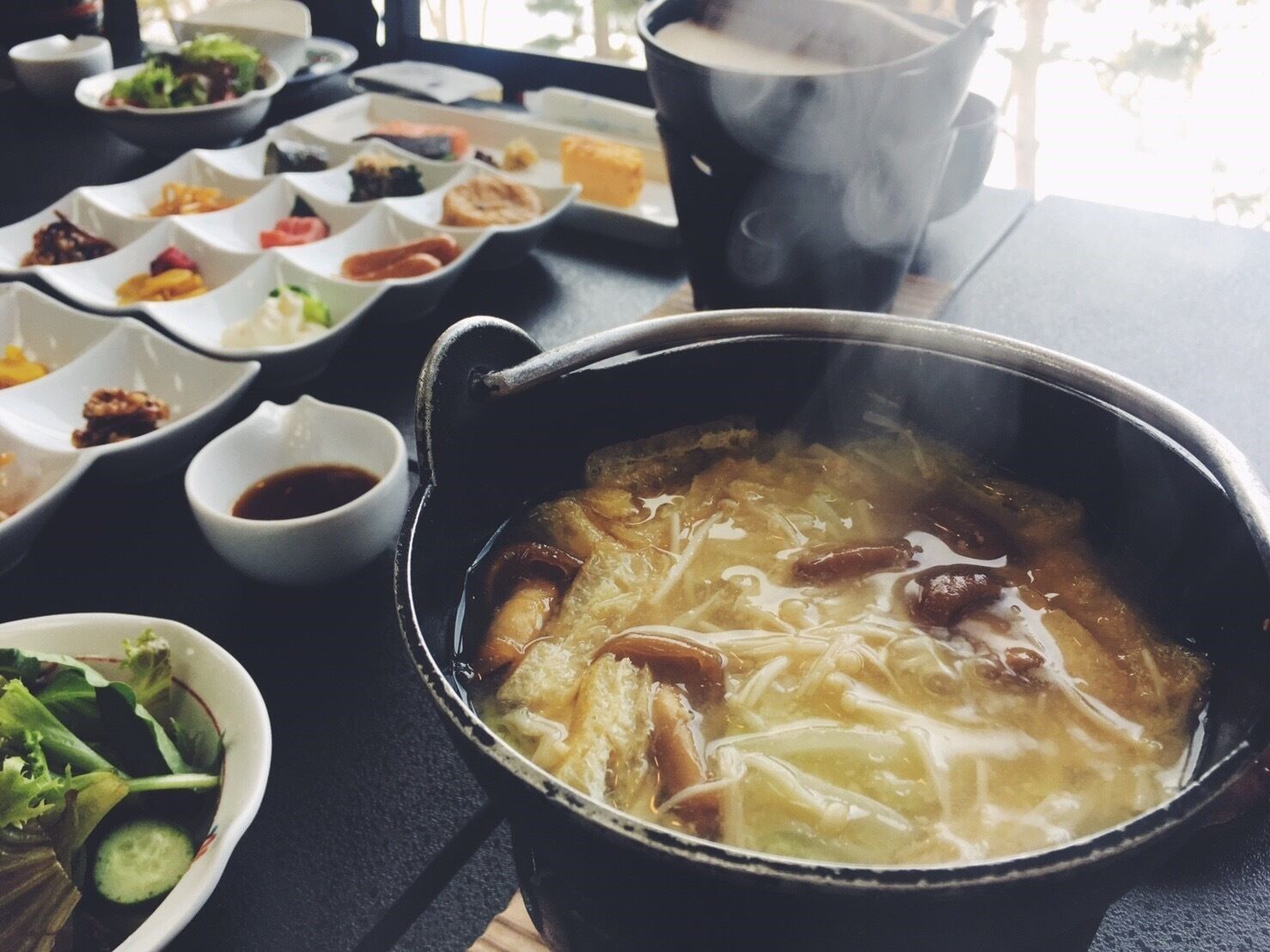 A hot pot meal with various side dishes and a steaming pot.