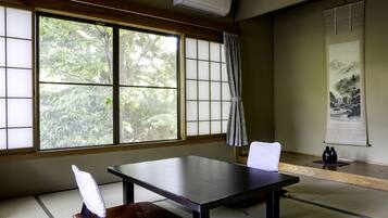 A traditional Japanese room with tatami flooring, a low table, and a view of trees through large shoji screens.
