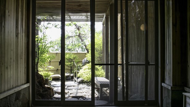 Ein traditioneller japanischer Raum mit Tatami-Böden, niedriger Holzbalkendecke und Blick auf einen Garten durch eine Schiebetür.