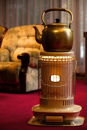 A brass teapot with a handle and spout, placed on a white stand with a wire cage around it. - Ryokan Warabino (Takayama)