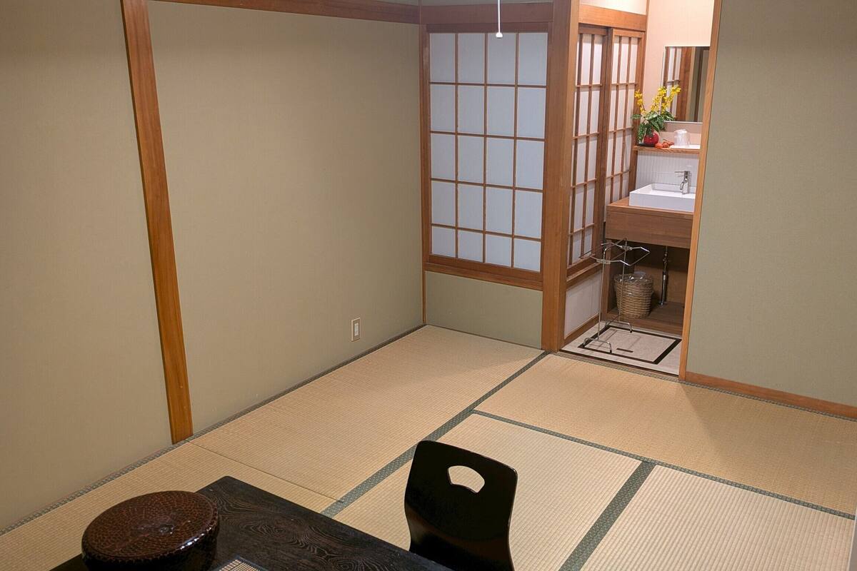 Una habitación japonesa tradicional con suelo de tatami, una mesa baja, una silla y un pequeño armario de madera.