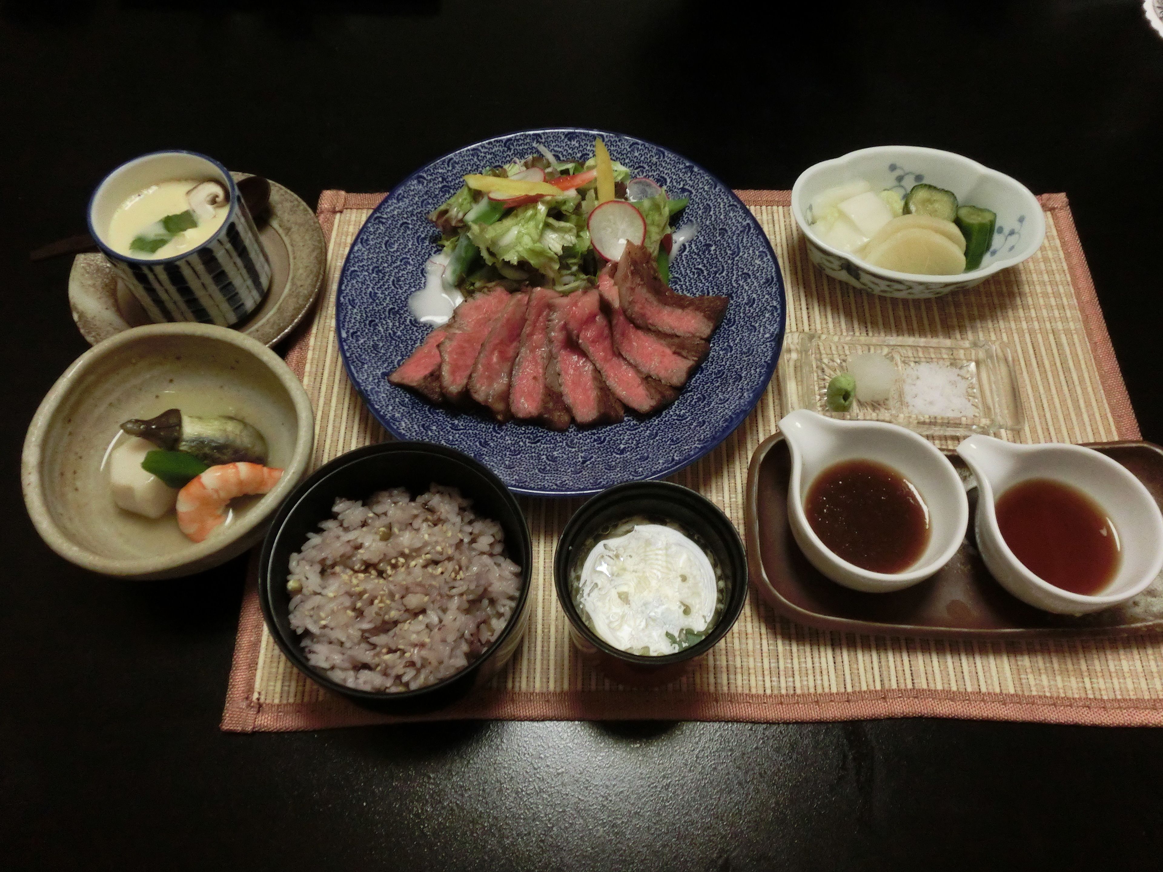 Una mesa con un plato de carne en rodajas, verduras y arroz, acompañado de recipientes pequeños con salsas y una taza de té.