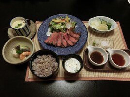 Una mesa con un plato de carne en rodajas, verduras y arroz, acompañado de recipientes pequeños con salsas y una taza de té.