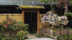 Ein traditionelles japanisches Gebäude mit Holzeingang, einem Kiesweg und einem Schild mit japanischen Schriftzeichen.