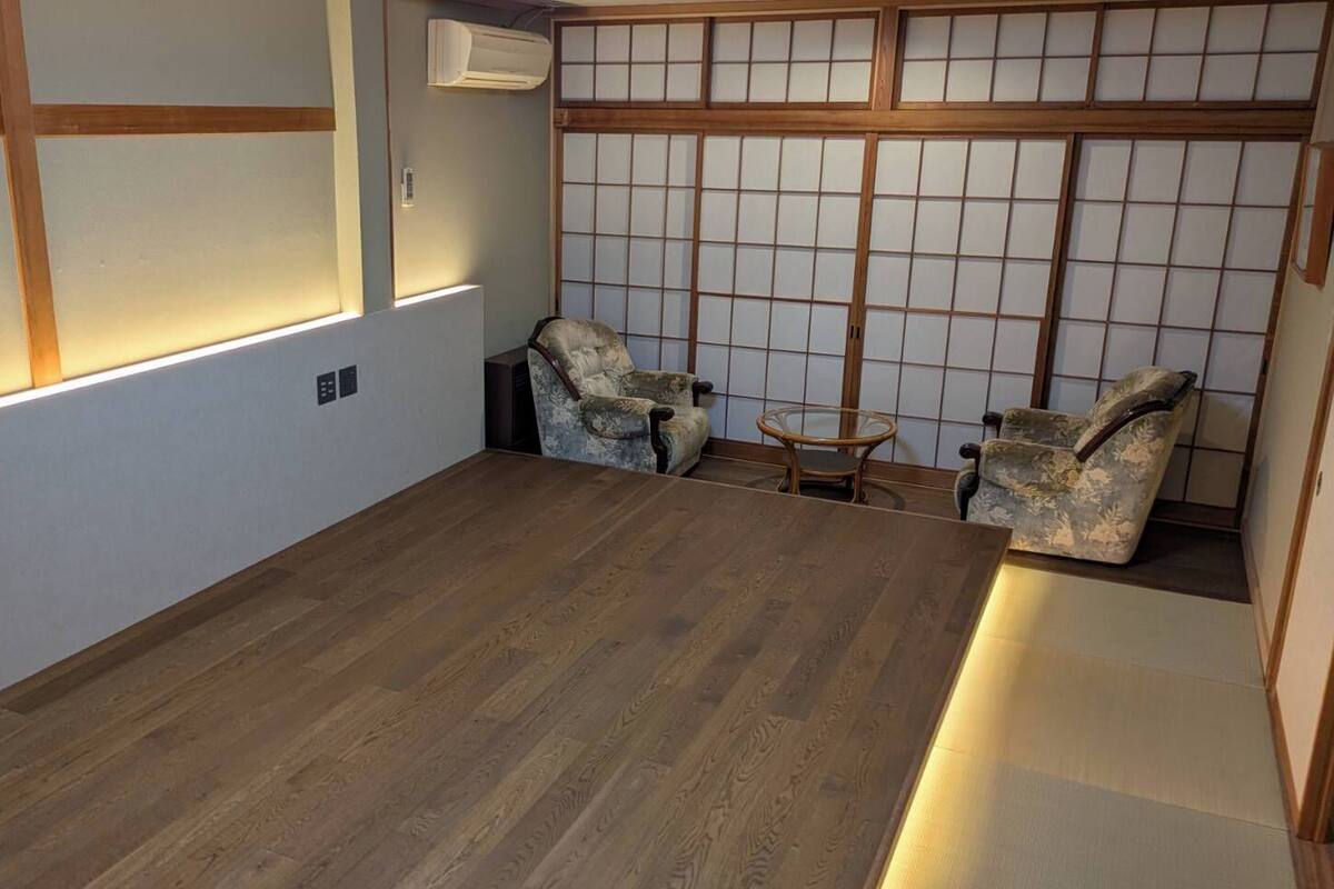 Una habitación con piso de madera, pared de esteras de tatami y dos sillas de tatami.