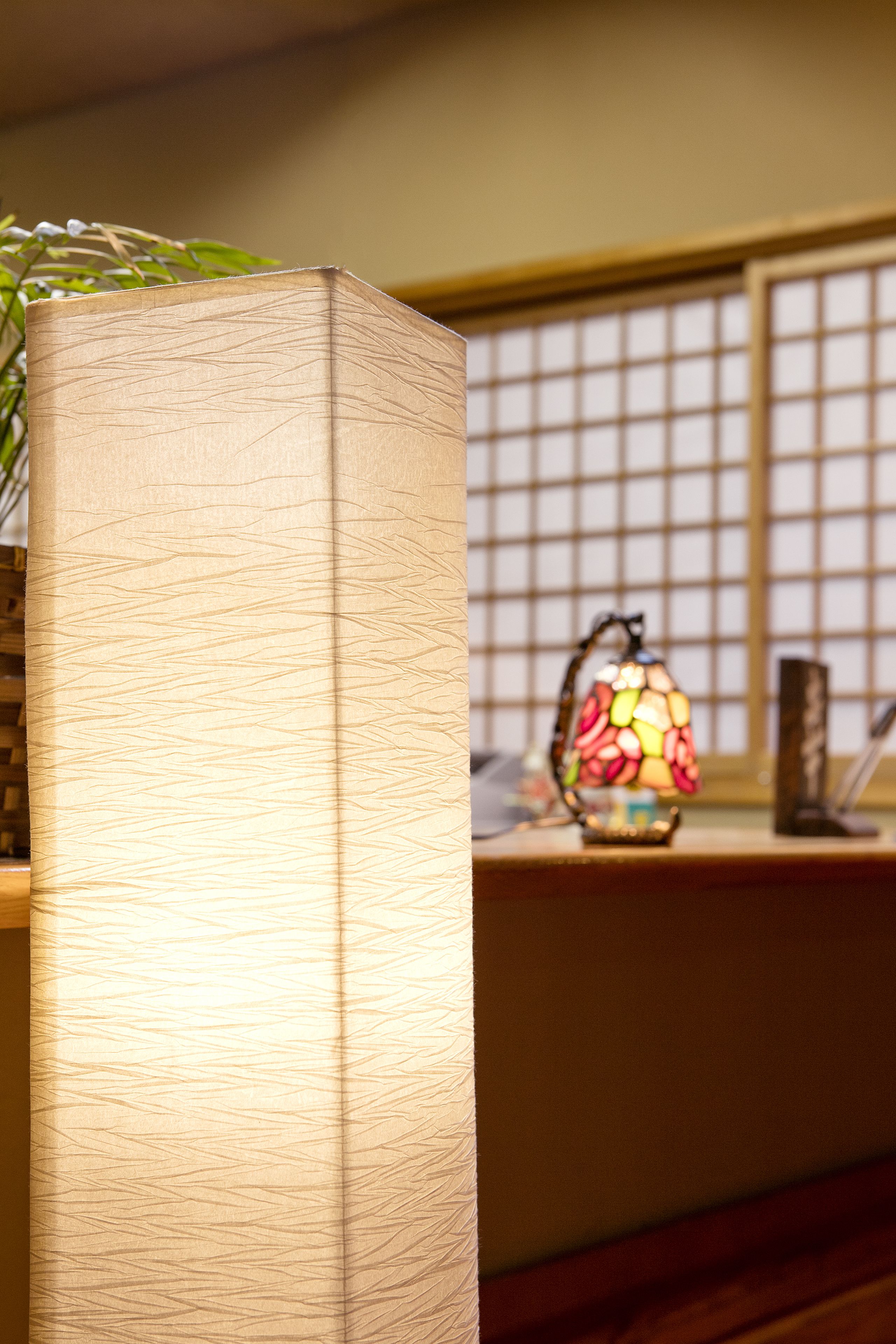 A wooden cabinet with a textured surface, a stained glass lamp, and a traditional Japanese screen in the background.