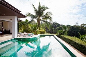 A swimming pool with a view of palm trees and a building with a covered patio area. - Baan Phukhao (Krabi)