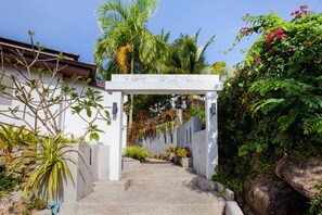 A concrete staircase leading up to a white archway, surrounded by lush greenery and plants. - Baan Phukhao (Krabi)