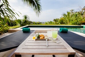 A wooden table with a plate of food, a glass of drink, and a flower. - Baan Phukhao (Krabi)
