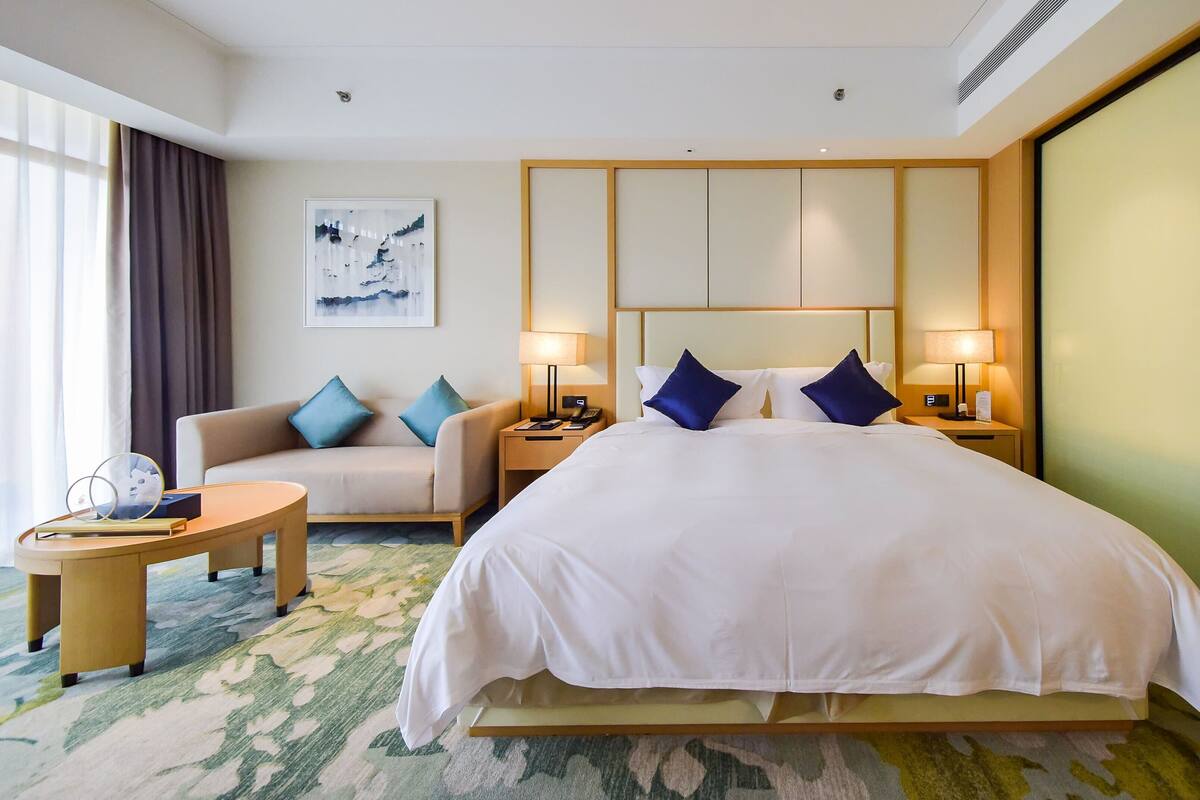 Een hotelkamer met een groot bed, een bank, een kleine tafel en een aan de muur bevestigde televisie.