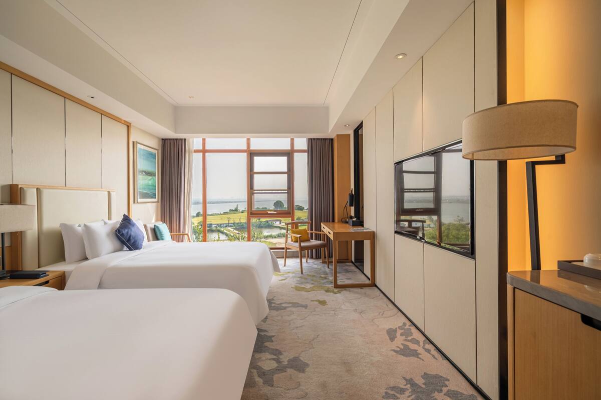 Hotelkamer met twee bedden, een bureau, een televisie en een groot raam met uitzicht.