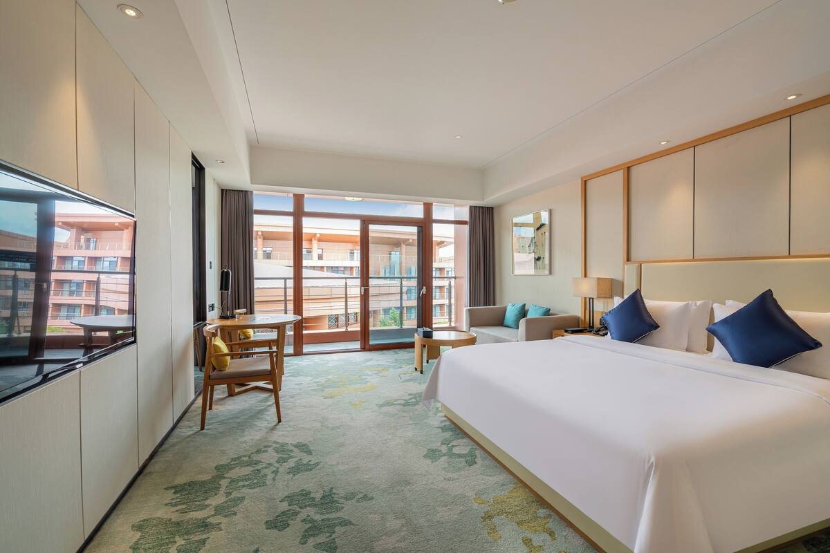Een hotelkamer met een groot bed, een bureau, een bank en uitzicht buiten.
