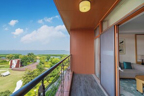 A balcony with a view of a body of water and greenery, a sliding glass door to a room with a sofa and a small table, and a ceiling light fixture.