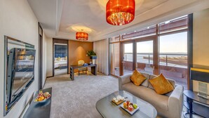 Une chambre d’hôtel moderne dotée d’une grande fenêtre, d’un canapé, d’une table basse avec des fruits, d’un bureau et d’une télévision.