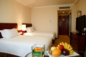 A hotel room with two beds, a television, and a fruit bowl on the table.