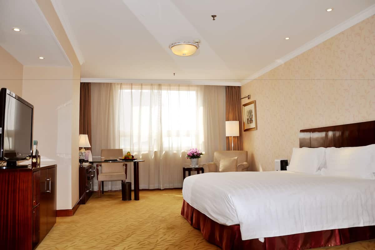 Een hotelkamer met een groot bed, een bureau met stoel, een televisie en een raam met gordijnen.