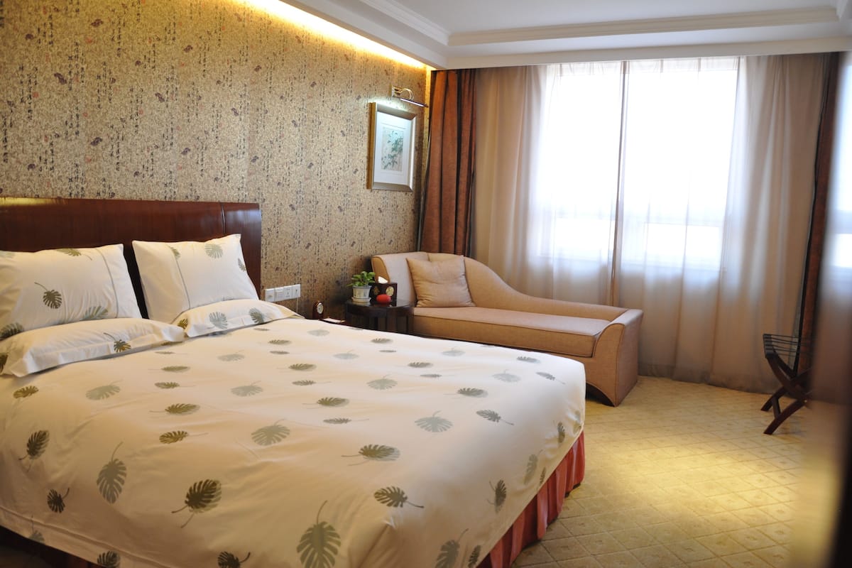 Een hotelkamer met een groot bed, een bank, een kleine tafel met een lamp en een raam met gordijnen.