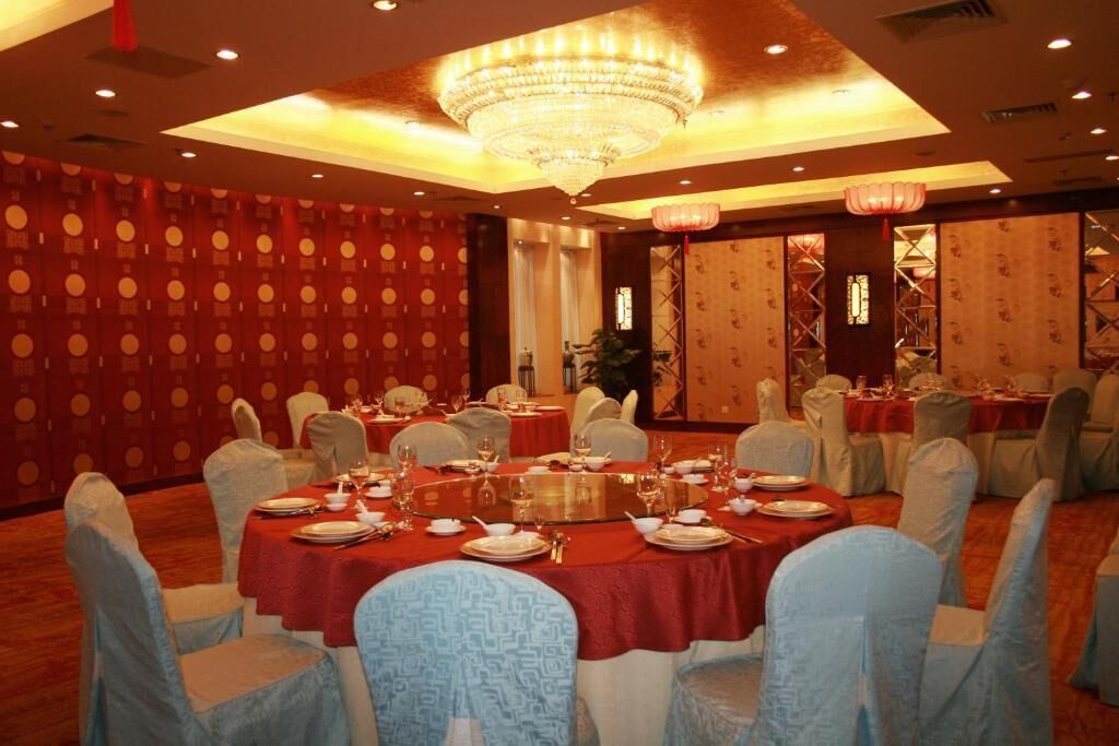 Un salón de banquetes con mesas redondas dispuestas para cenar, una gran araña y decoración tradicional.