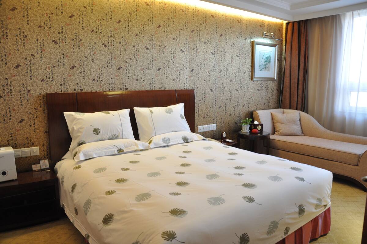 Een hotelkamer met een groot bed, een slaapbank, een nachtkastje en een aan de muur hangend schilderij.
