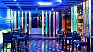 A modern bar with neon lights, high stools, and a bar counter.
