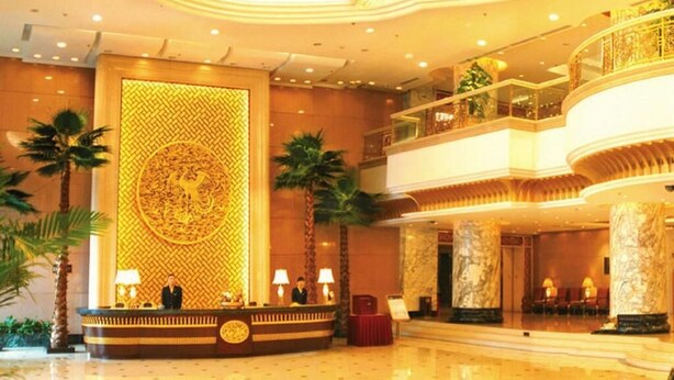 A grand lobby with a reception desk, palm trees, and a large decorative wall.