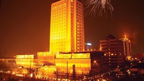 A high-rise hotel with multiple floors, illuminated by warm lighting, and a fireworks display in the background.