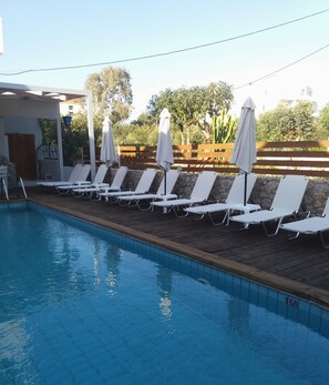 A swimming pool with lounge chairs and umbrellas, surrounded by a wooden deck and stone walls. - Naiades Almiros River Hotel (Agios Nikolaos)