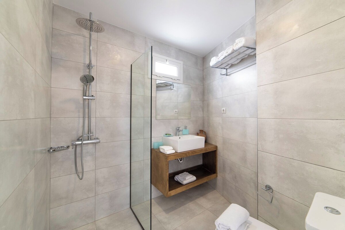 A bathroom with a glass-enclosed shower, a wooden vanity with a sink, and a towel rack.
