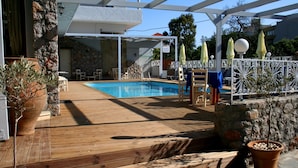 A wooden deck with a pool, outdoor seating, and potted plants. - Naiades Almiros River Hotel (Agios Nikolaos)