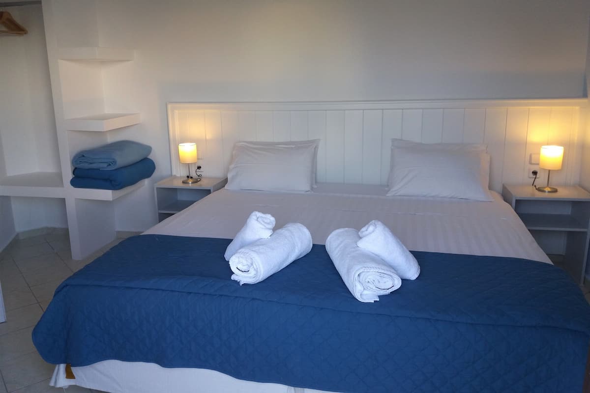 A neatly made bed with two rolled towels, white bedding, and two bedside lamps.