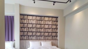 Un dormitorio con una gran estantería, una cama con ropa blanca y una cortina morada.